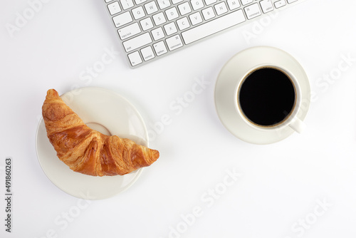 Top view of keyboard, croissant and cup of coffee on white background