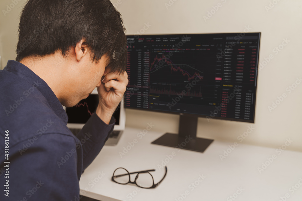 Stressed young businessman, trader or investor touch head, disappointed when bad investment or economic crisis, losing money from investing, trading stock, Cryptocurrency as Bitcoin on laptop at home.