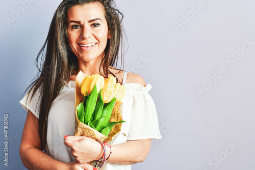 Attractive pleased  Lovable  Beautiful Smiling  Grateful  Woman receives flowers as present, stands with closed eyes, enjoys her favorite   Yellow, isolated on  purple background. Romantic portrait.