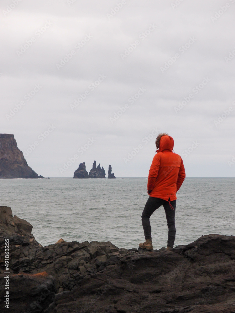 Iceland landscape photo of man in a red jacket in front of Reynisfjara black-sand beach found on the South Coast of Iceland.