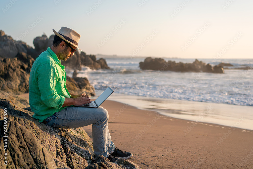 man sitting with a laptop alone at the beach.