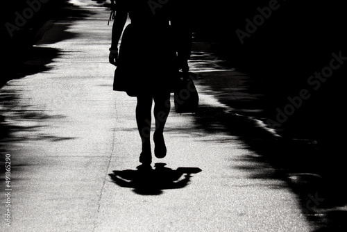 Silhouette and shadow of lonely woman walking with handbag on a street. Female legs on a sidewalk, concept of depression, quarantine in the city during coronavirus pandemic