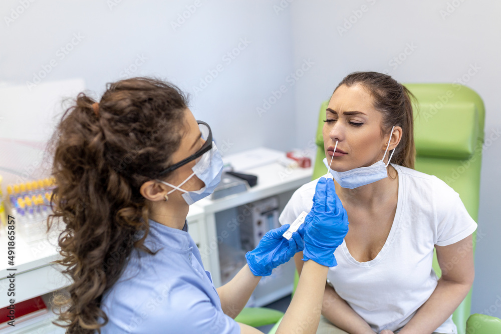 Female patient being tested for Covid-19 with a nasal swab, by a health Professional protected with gloves and PPE suit. Rapid Antigen Test during Coronavirus Pandemic. Female patient being tested for Covid-19 with a nasal swab, by a health Professional protected with gloves and PPE suit. Rapid Antigen Test during Coronavirus Pandemic.