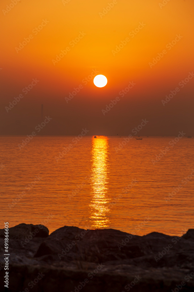 amazing colorful clouds on sunset. Beautiful golden sunset in the sea with saturated sky and clouds. Reflection in the water. Rocky coastal line. Peaceful serene landscape. Nature background.