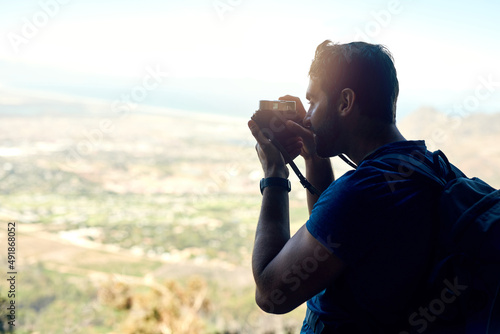 Its quite magical up here. Rear view shot of a young man taking a photo of the scenic view from the top of a mountain.