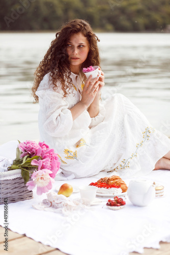 A girl with curly hair, in a white dress, serving cup of a tea, a croissants at a picnic, outside, in sunny time. photo