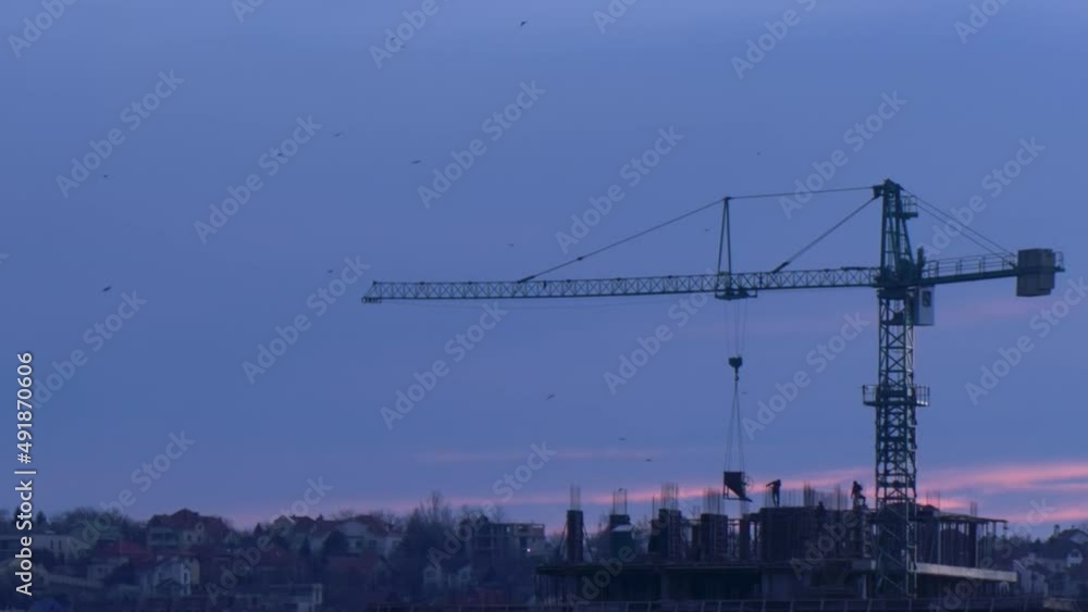 Construction workers at a building site with crane at sunset Construction workers at a building site with crane at sunset