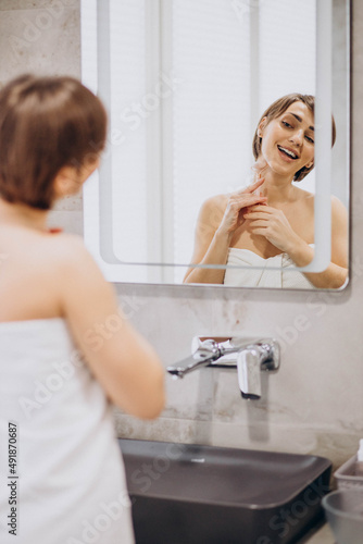 Young woman looking into the mirror and using jade face roller at home