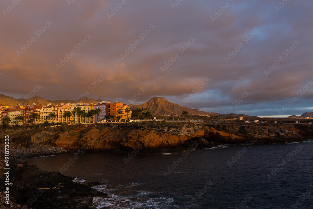 Panoramic view of the Illuminated Las Americas at night against the colorful sunset sky with lights on the horizon on Tenerife island, Spain
