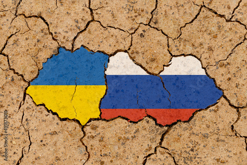 Russia vs Ukraine national flags grunge pattern on grungy dry cracking parched earth. Cracked soil