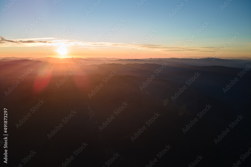 Aerial view of dark mountain hills with bright sunrays of setting sun at sunset. Hazy peaks and misty valleys in evening Aerial view of dark mountain hills with bright sunrays of setting sun at sunset. Hazy peaks and misty valleys in evening