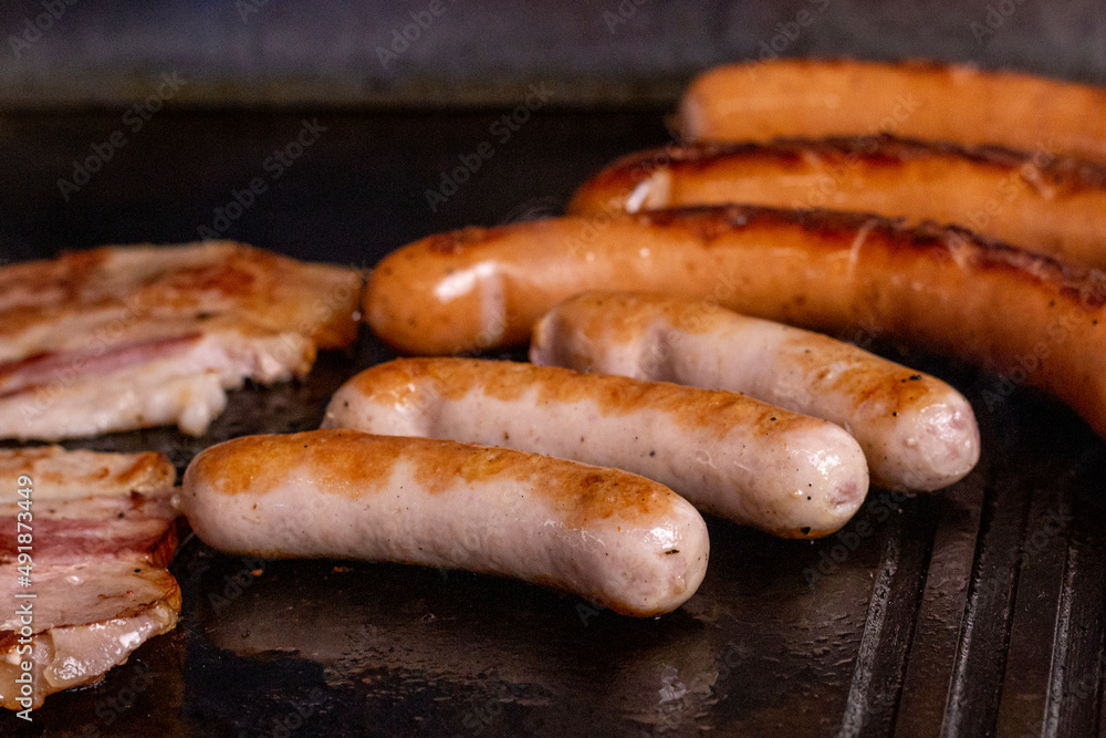 Grilled crispy smoked bacon and sausage on barbecue with steam. close up image. Fast food, bbq, grill. Grilled crispy smoked bacon and sausage on barbecue with steam. close up image. Fast food, bbq, grill.