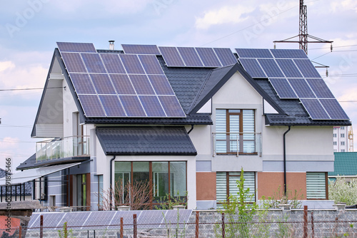 Residential house with rooftop covered with solar photovoltaic panels for producing of clean ecological electrical energy in suburban rural area. Concept of autonomous home