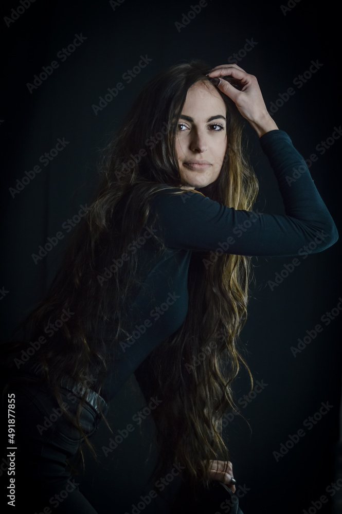 Portrait of a beautiful young Italian woman with very long hair leaning forward who is fixing her hair with her hand Portrait of a beautiful young Italian woman with very long hair leaning forward who is fixing her hair with her hand
