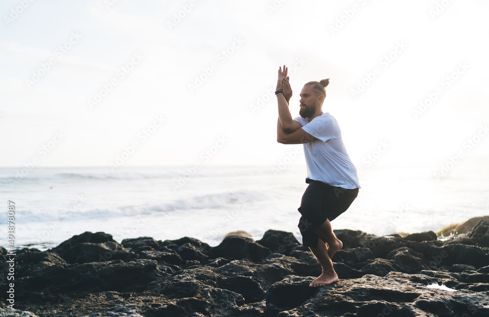 Caucaisan man in sportswear stretching body muscles enjoying recreation balance retreat at rocky coastline, young male yogi have workout training for feeling appeasement and mindfulness outdoors