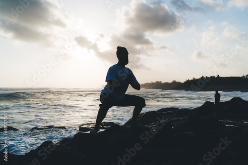 Silhouette of Caucaisan male in balance asana praying and breathing during holistic retreat practice at seashore, man spending weekend evening for training and keeping sportive lifestyle