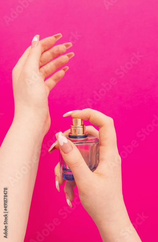 female hands with perfume bottle on pink background