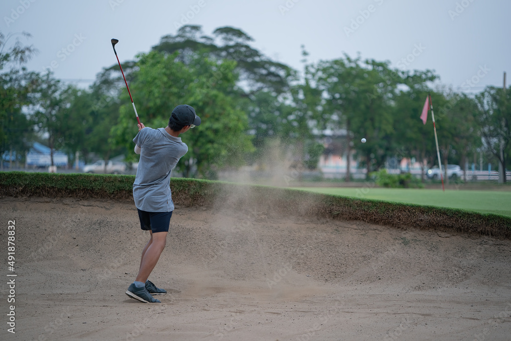 Boy golf player chipping from sand bunker onto green.