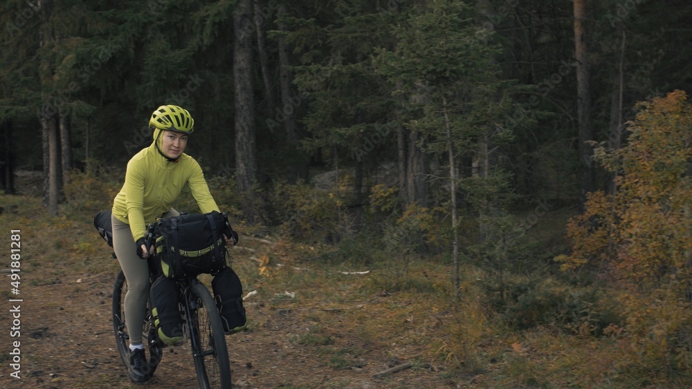 Obraz premium The woman travel on mixed terrain cycle touring with bike bikepacking outdoor. The traveler journey with bicycle bags. Stylish bikepacking, bike, sportswear in green black colors. Magic forest park.