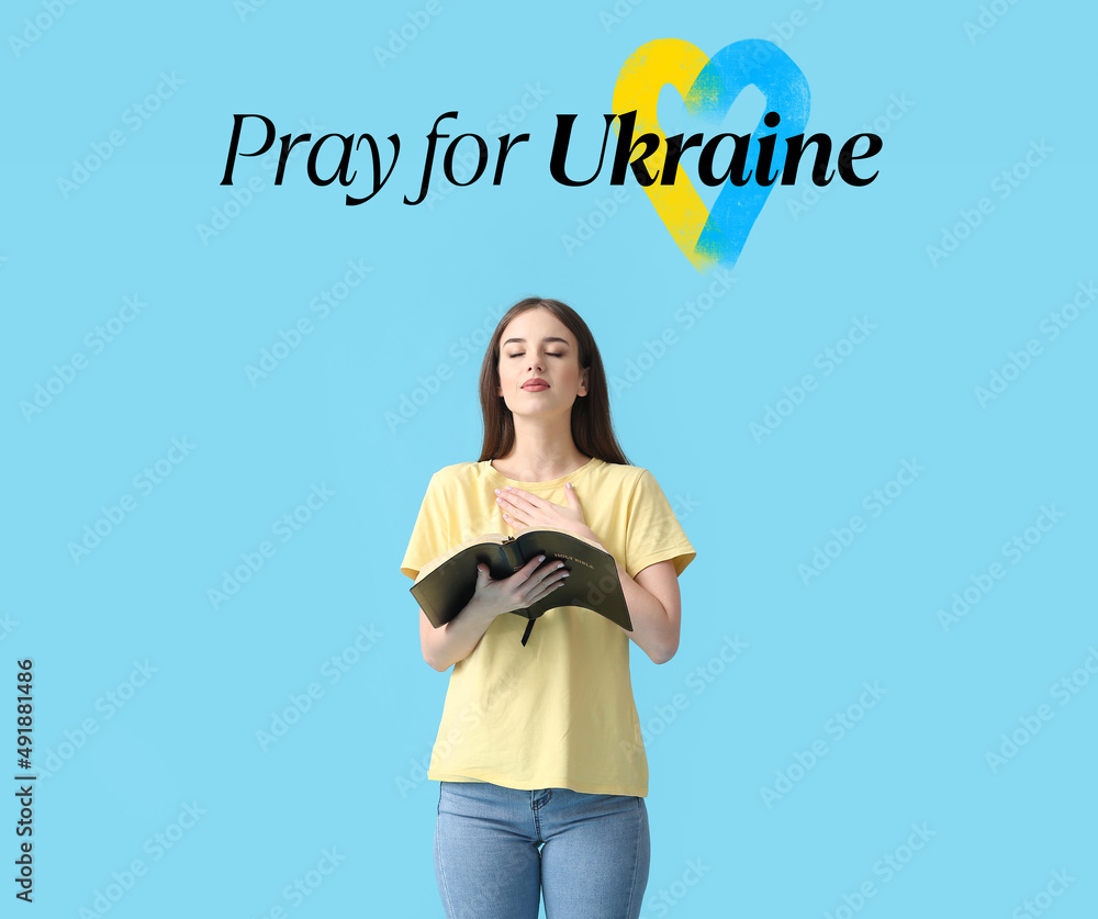 Young woman with Bible and text PRAY FOR UKRAINE on blue background Young woman with Bible and text PRAY FOR UKRAINE on blue background