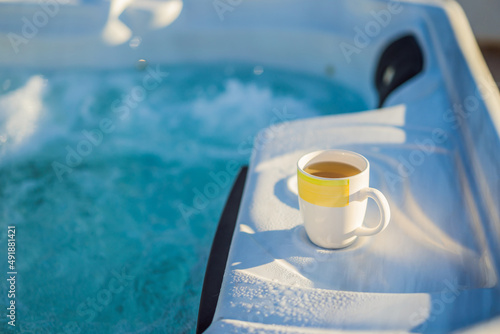 Mug with morning drink on the side of Hot tub hydromassage pool. Illuminated pool. Rest outside the city. Cottage with hydromassage pool