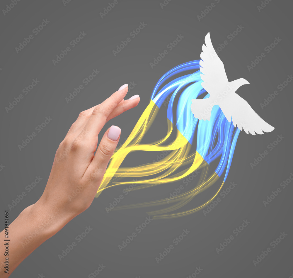 Fototapeta premium Female hand and paper dove on grey background. Stop the war in Ukraine