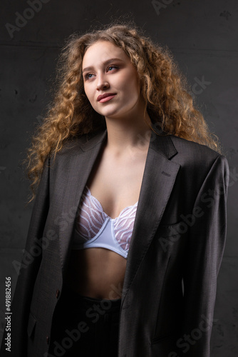 Portrait of a young red-haired curly sexy girl in a jacket with long hair in the studio. Dramatic photo in dark colors.