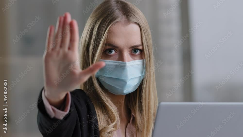 Portrait in office caucasian girl woman in medical face mask with laptop angry looking at camera puts palm forward no stop war gesture prohibition fence defense limit keep distance sign pandemic rules Portrait in office caucasian girl woman in medical face mask with laptop angry looking at camera puts palm forward no stop war gesture prohibition fence defense limit keep distance sign pandemic rules