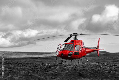 Red Helicopter landed near Thrihnukagigur Volcano in Iceland on a Lava field near Bláfjöll Country Park and Reykjavik for tourists. Modern aviation in contrast with archaic colorless scenery.