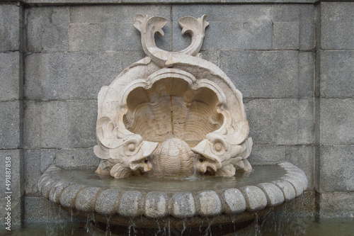 historic stone fountain with two fish and a shell in a street in Madrid. Spain