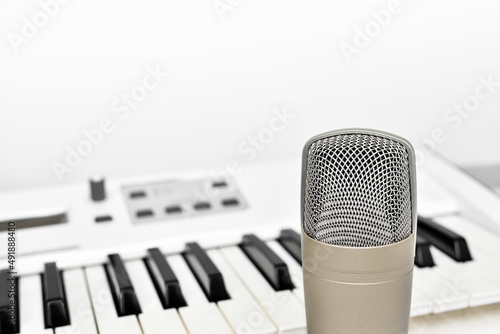 Fotografie Professional studio microphone for voice and music recording against blurred synthesizer keyboard background with copy space