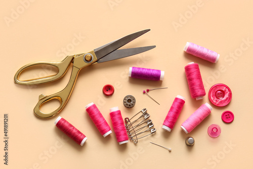 Thread spools with scissors, buttons and pins on beige background