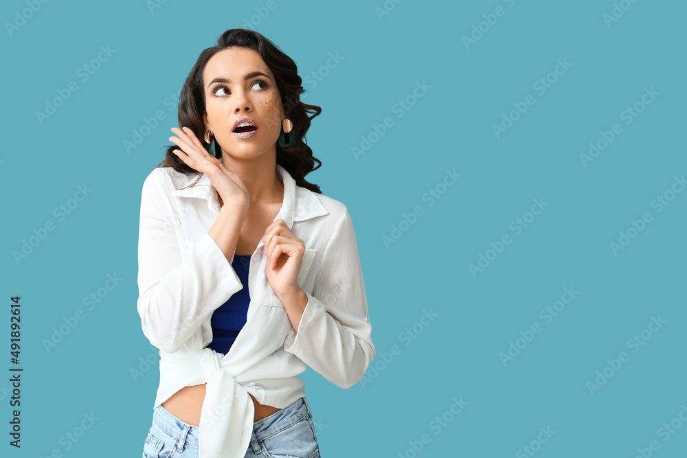 Attractive young woman with glitters on her face against blue background Attractive young woman with glitters on her face against blue background
