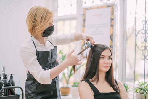 Professional hairdresser woman in an apron makes a haircut to a young girl in a beauty salon.