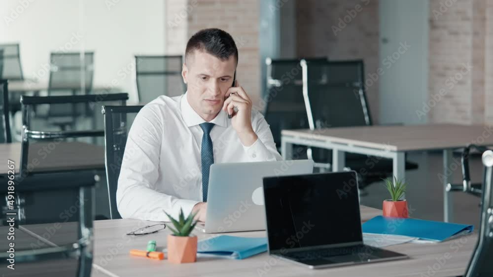 focused businessman has phone negotiations wearing white shirt and tie sitting at the workplace looking on screen laptop working in the office focused businessman has phone negotiations wearing white shirt and tie sitting at the workplace looking on screen laptop working in the office