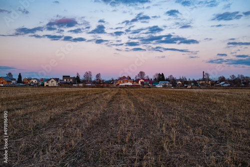 Rural view. Cutted grass in the field. Evening yellow light. Country houses and sunset sky on background.
