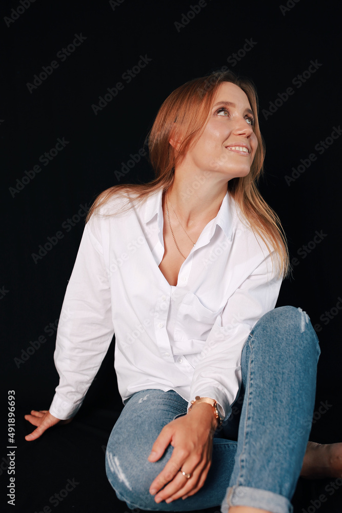 Beautiful Ukrainian girl in a photo studio. Portrait of a cute girl on a black background. woman in jeans and white shirt. Classic portrait in the studio. White chair-ladder. Portrait about life Beautiful Ukrainian girl in a photo studio. Portrait of a cute girl on a black background. woman in jeans and white shirt. Classic portrait in the studio. White chair-ladder. Portrait about life