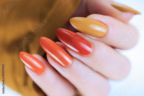 Canvas Print Female hand with long nails and a bottle of bright red orange yellow nail polish