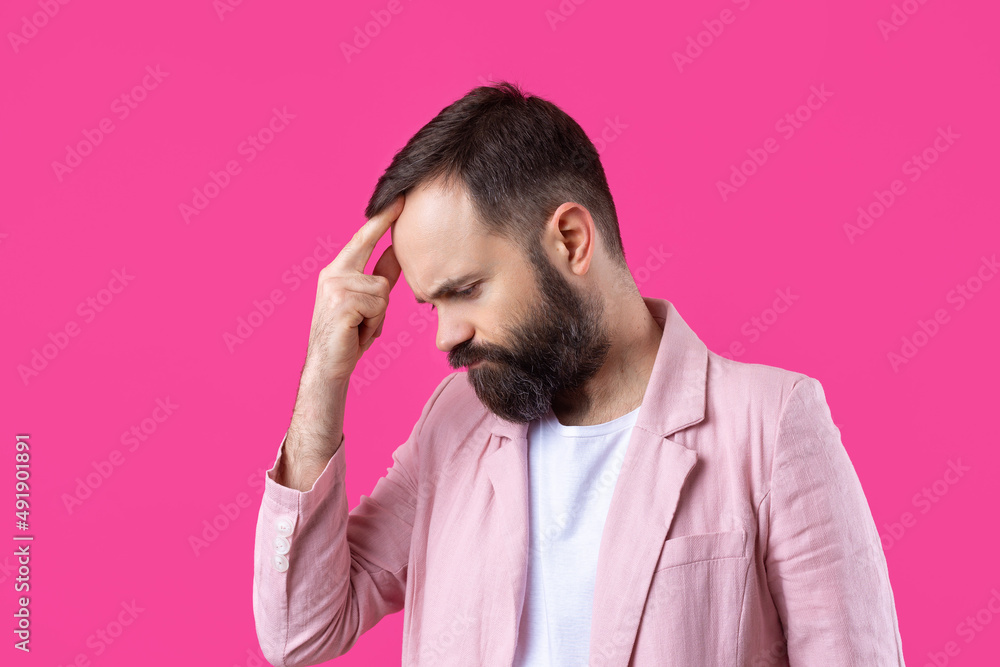 Handsome man with a beard in a pink jacket is thinking over an isolated red background. Handsome man with a beard in a pink jacket is thinking over an isolated red background.