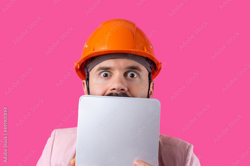 Portrait of young construction engineer wear orange hard hat, in a pink jacket standing on red studio background. A man with a tablet in his hands. Portrait of young construction engineer wear orange hard hat, in a pink jacket standing on red studio background. A man with a tablet in his hands.