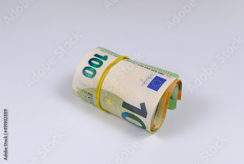 Money roll tightened with rubber band on white background. Rolled euro banknotes
