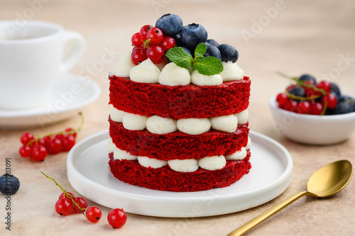 Mini red velvet cake decorated with berries and mint. Portion cake on a white plate with a cup of tea. selective focus 