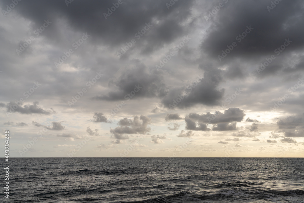 horizontal landscape view of a backdrop of calm ocean water under an expressive and cloudy sky
