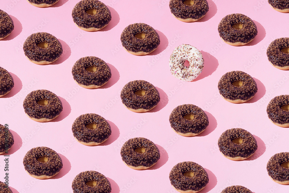 Fototapeta premium Arranged ring donuts with chocolate and white glaze and small colorful crumbs on a pink pastel background. Pattern.