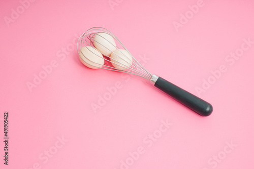 Whisk and raw eggs on pastel pink. Light banner background, copy space for text. Culinary mixer, whipping egg white and yolk, preparing and mixing cream. © lagano