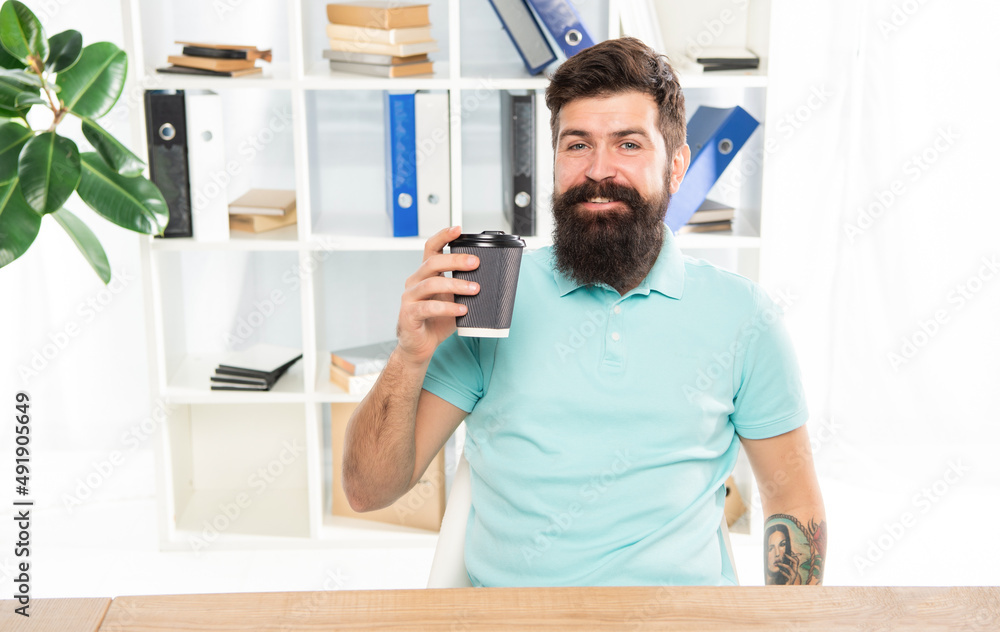 Fototapeta premium Happy man holding takeaway coffee cup sitting in office, coffee break