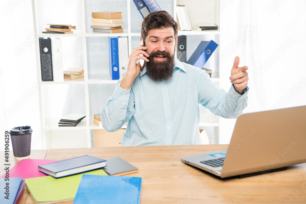Happy guy talking on mobile phone working on laptop in office, business call Happy guy talking on mobile phone working on laptop in office, business call