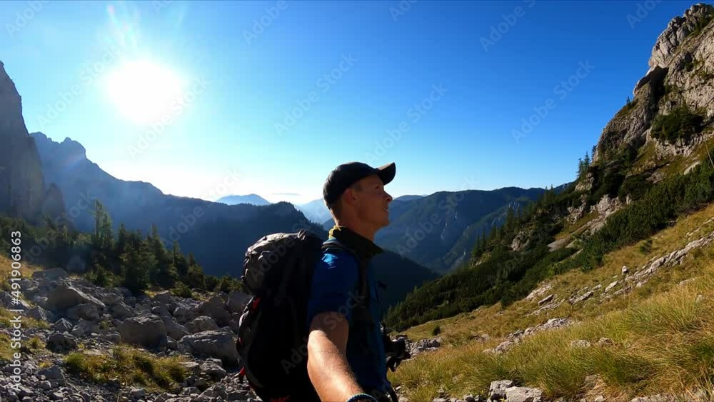 Man with backpack filming himself while hiking to the summit of Hinterer Polster in the scenic region of the Hochschwab mountain in Styria, Austria. Alpine meadows and sharp rocks. Hike concept. Free
