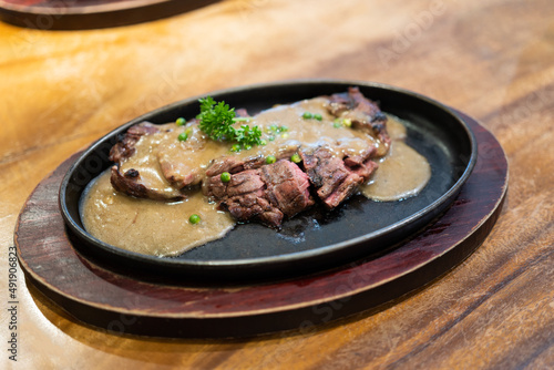 Grilled Juicy steak medium rare beef with herbs and spices on pan hot topped with black pepper sauce on wooden table.