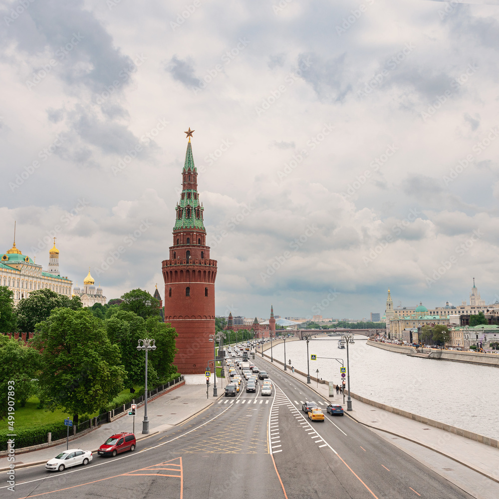 Embankment of the Moscow River with many cars. The towers of the Moscow Kremlin against the background of a cloudy spring sky